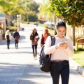 A street in daylight with people with pedestrians looking at their phones as they walk with a young woman in the foreground.